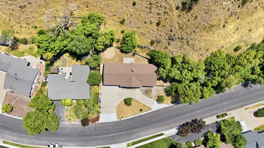 Residential property featuring a spacious lot with mature trees, a paved driveway, and a shingle roof