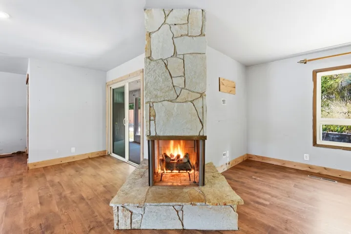Central stone fireplace with hearth, wood-finish flooring, white walls, and a sliding glass door