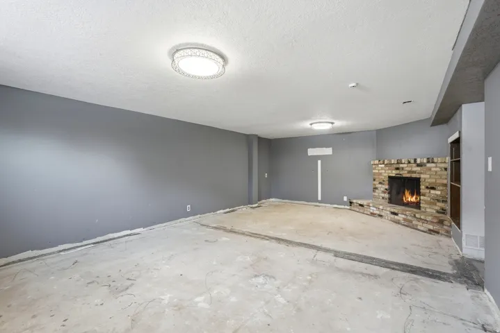 Spacious interior with an exposed concrete floor, a brick fireplace with a hearth, and modern flush-mount lighting fixtures