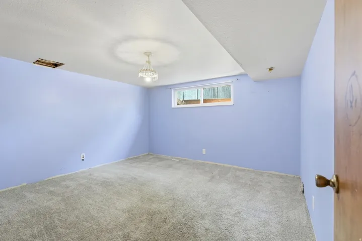 Spacious room featuring light blue walls, gray carpet, and a window with exterior visibility