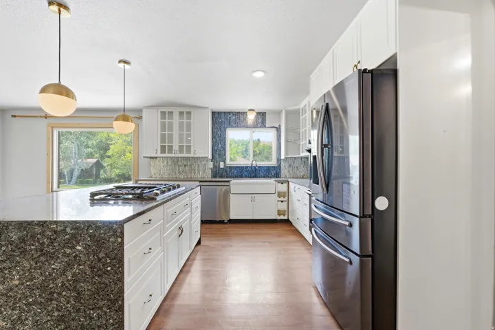 Spacious kitchen featuring a large island with a built-in gas cooktop, white shaker-style cabinetry, dark stainless steel appliances, and wood-finish flooring