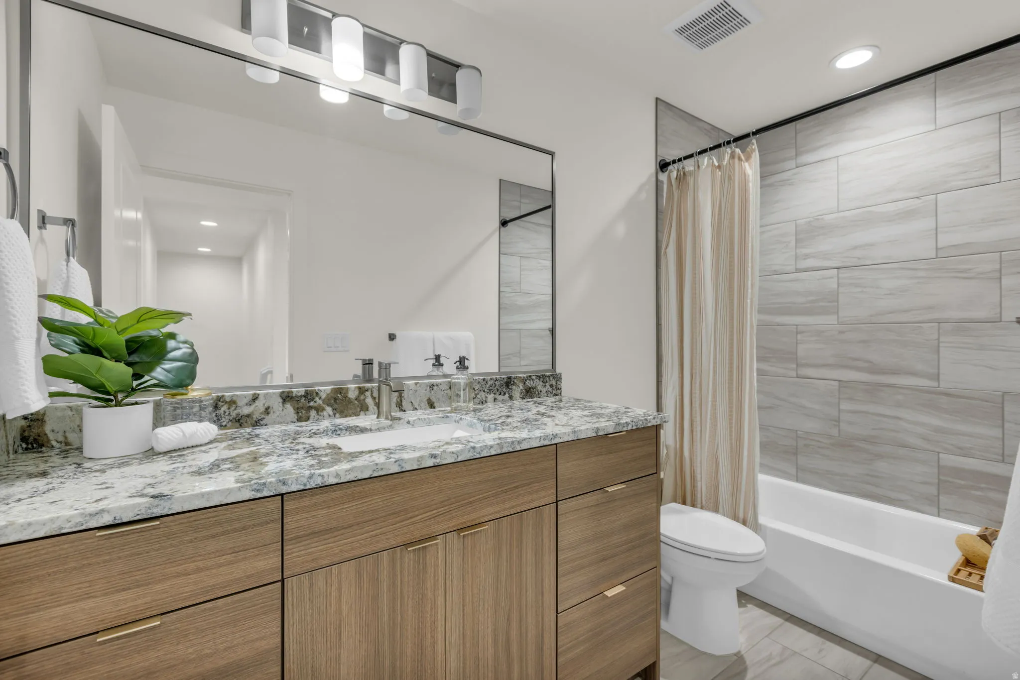Wood-finish vanity with gold-tone hardware, a large rectangular mirror, and a sleek light fixture