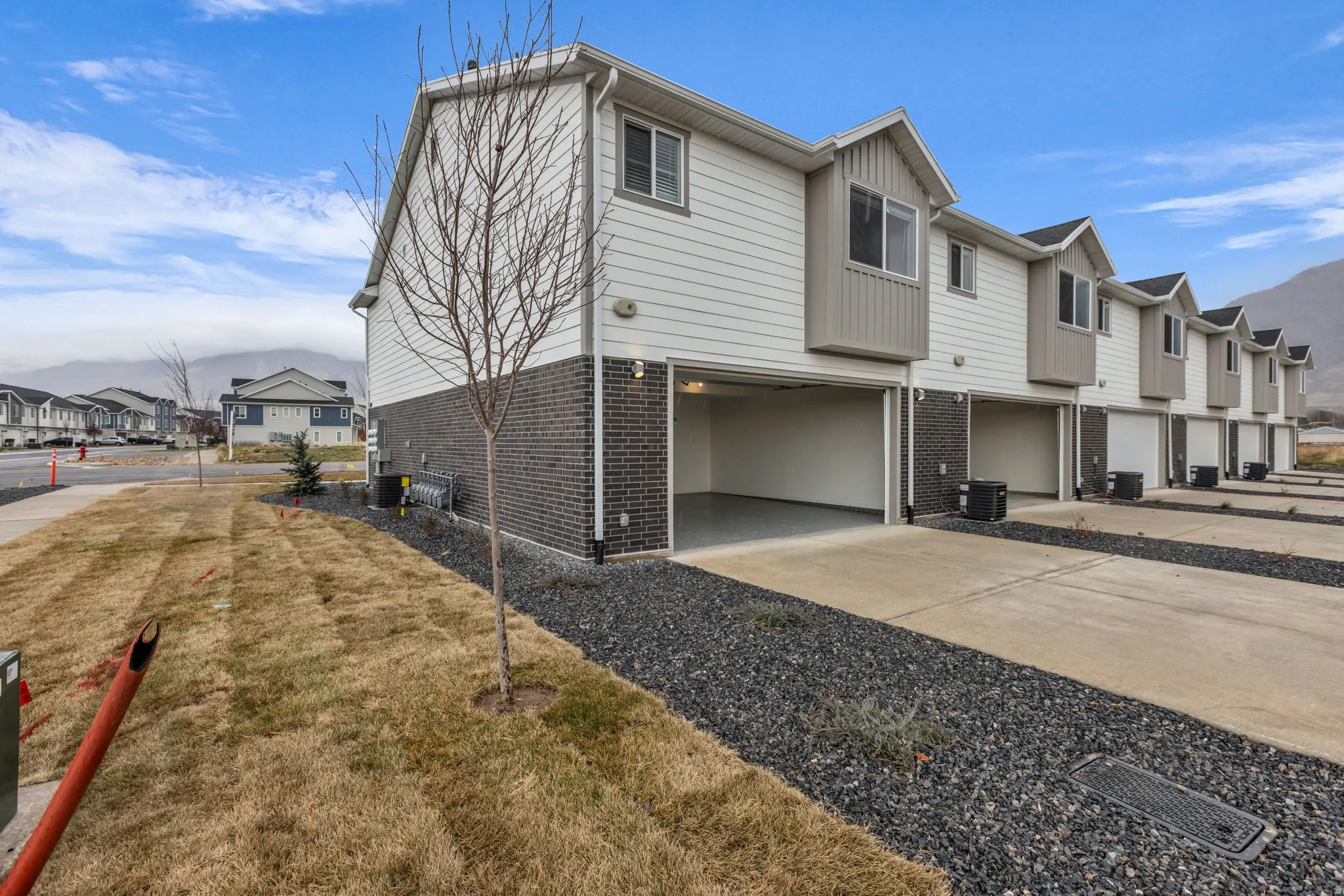 Contemporary townhome exterior featuring white siding, dark brick accents, and a two-car garage with concrete driveway
