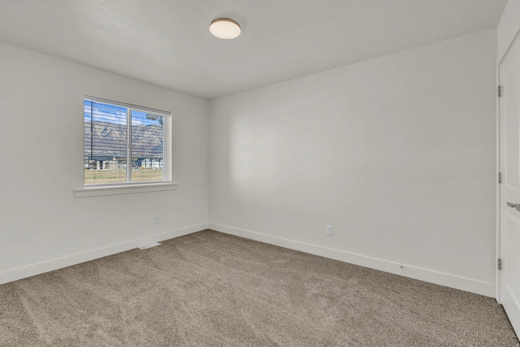 Bright interior space with neutral-toned carpet, white walls, and a single window