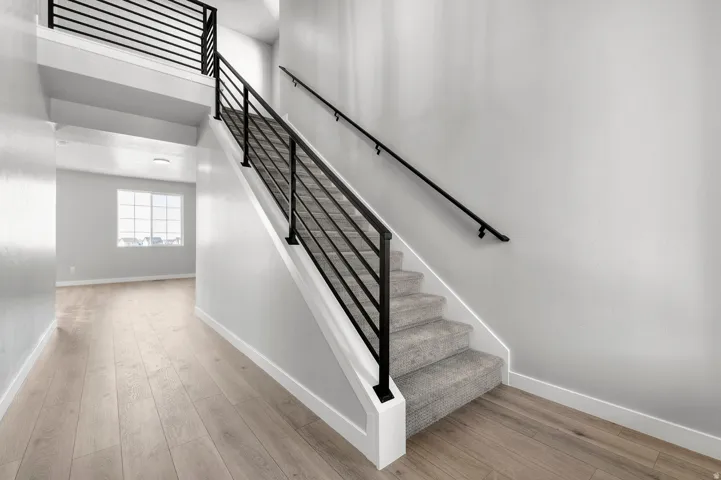 Staircase featuring dark metal balusters and handrails, white risers, and carpeted treads