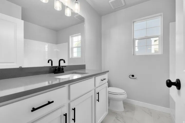 Bathroom featuring white shaker cabinetry, a gray countertop, an undermount sink with matte black fixtures, and a vanity light fixture