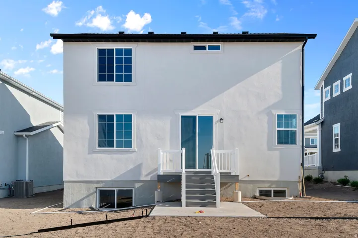 White stucco exterior featuring multiple windows, a sliding glass door, and a ground-level patio