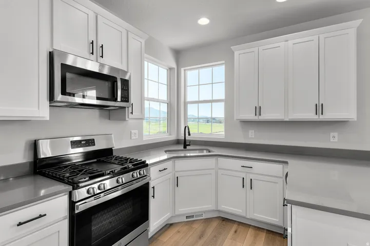 Modern kitchen featuring white shaker cabinetry, stainless steel appliances, and wood-finish flooring