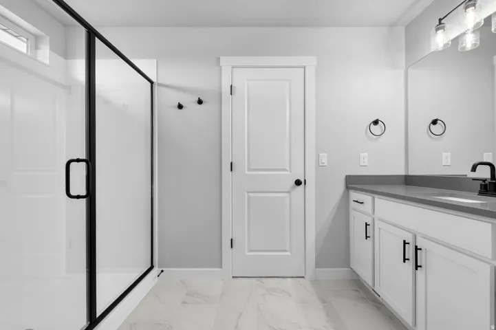 Full bathroom featuring a frameless glass shower enclosure with matte black trim, a white vanity with slab cabinet doors and matte black hardware, and a gray countertop