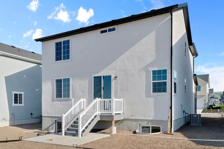 Rear exterior featuring light-toned stucco siding and a black shingle roof
