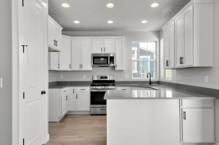 Kitchen featuring light wood-finish flooring, white cabinetry with black hardware, stainless steel appliances, and light gray countertops