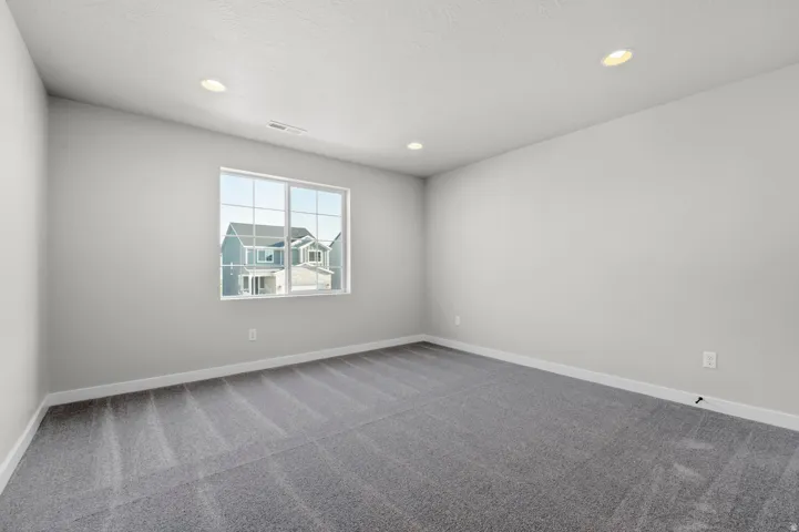 Room featuring a large white-framed window, neutral gray walls, recessed lighting, and gray patterned carpeting