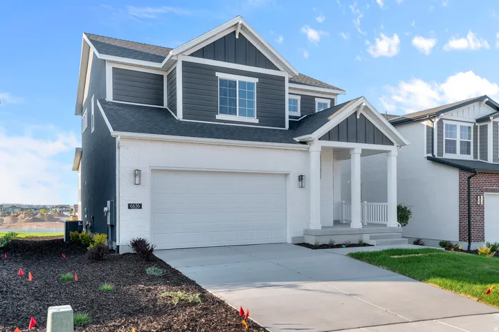 Two-story home with a two-car garage, featuring a covered entry porch with columns, a combination of white brick and dark gray siding, and a landscaped front yard with a concrete driveway
