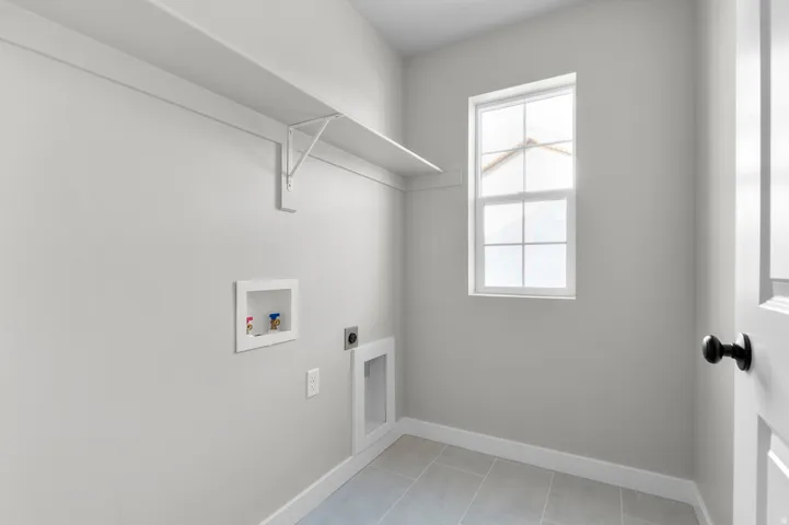 Utility room featuring light gray walls, tile flooring, a window, a white shelf, and a white paneled door with a black knob