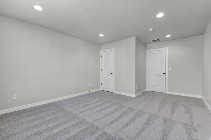 Spacious room featuring light gray walls, plush gray patterned carpet, white baseboards, and multiple recessed ceiling lights
