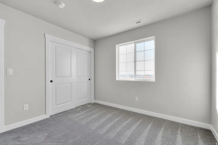 Carpeted room featuring light gray walls, a window with grid panes, and a closet with bifold doors