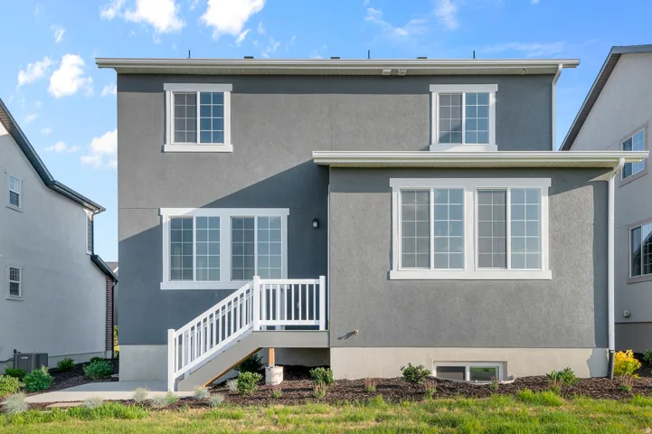 Rear exterior featuring grey stucco siding, white-framed windows, a walk-out deck with white railings, and a lower-level window well
