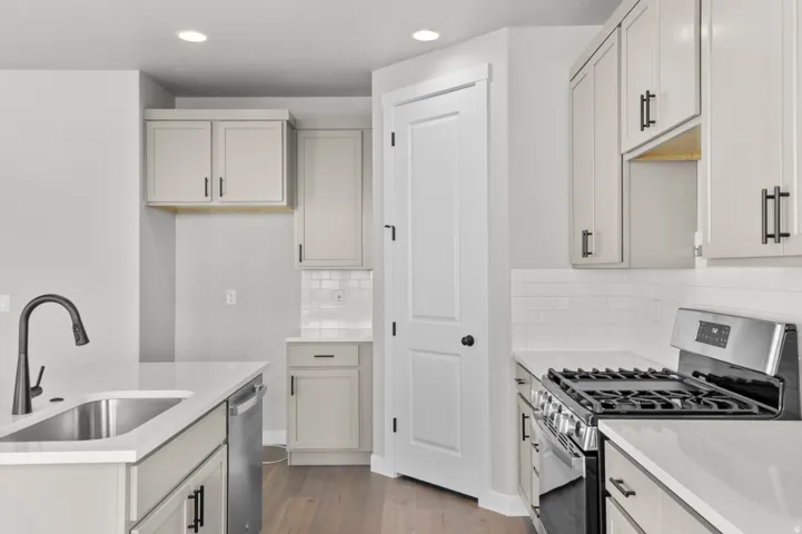 Modern kitchen featuring light gray cabinetry with black hardware, white countertops, stainless steel appliances, and wood-finish flooring