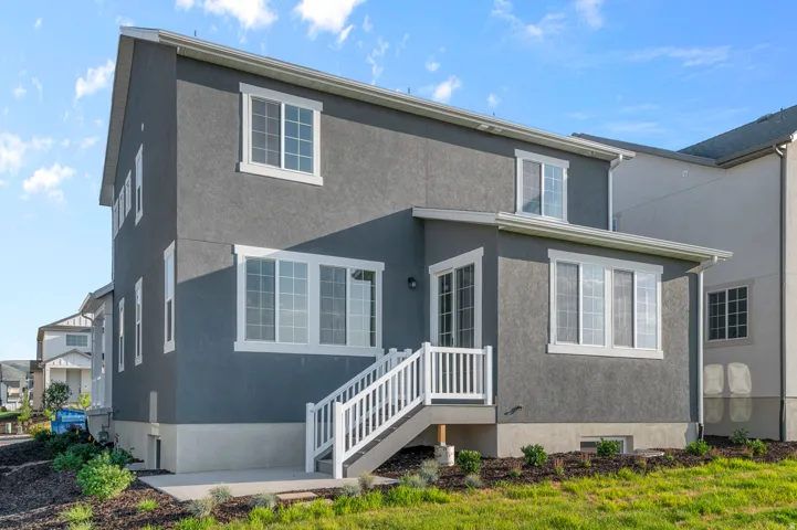 Rear exterior featuring a two-story design with stucco siding, white-framed windows, a ground-level patio, and a deck with stairs