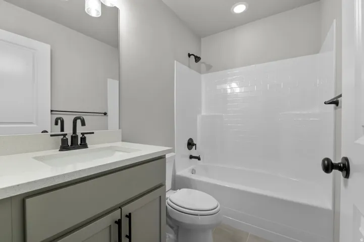 Bathroom featuring a white subway tile tub surround, dark bronze fixtures, a light gray vanity with a white countertop, and recessed lighting
