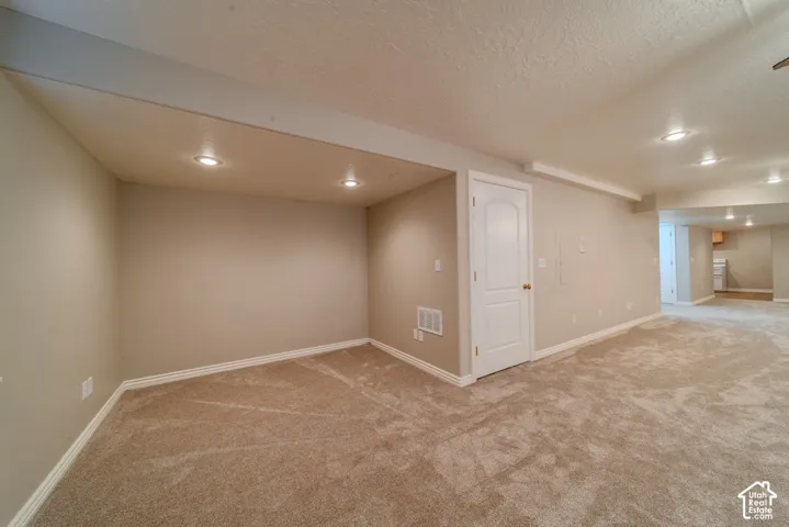 Expansive carpeted area with recessed lighting, neutral wall tones, white baseboards, and a white interior door