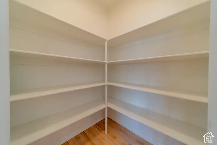 Corner pantry with multiple white shelving units and wood-finish flooring