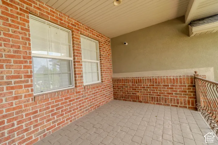 Covered outdoor patio featuring a brick facade, stucco wall, and a patterned paver floor