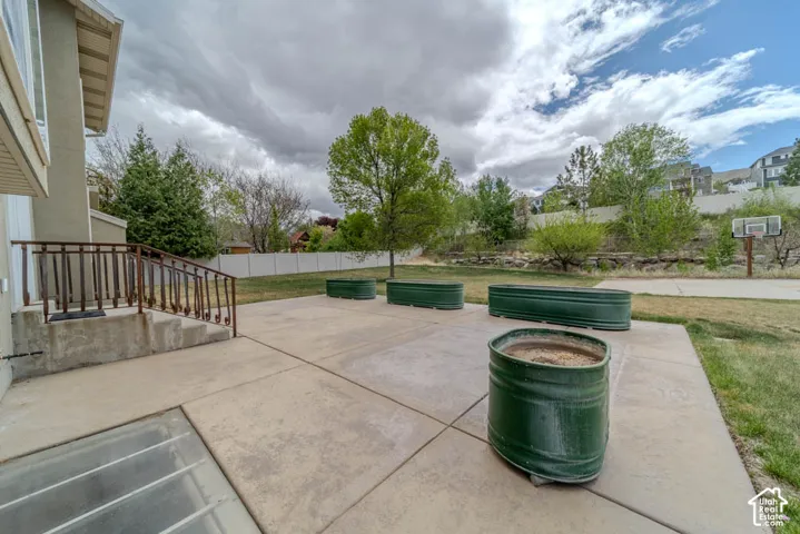 Expansive concrete patio with integrated stairs and metal railing, featuring a lower-level window well and a surrounding grassy area