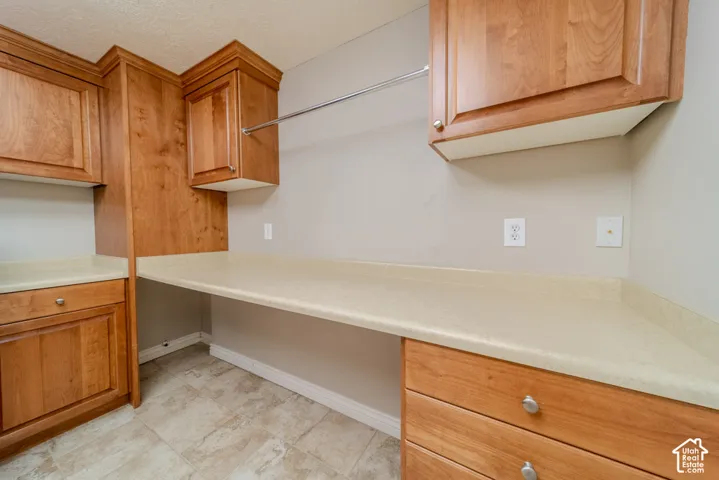 Light wood-finish cabinetry featuring crown molding, ample countertop space, a built-in hanging rod, and tile flooring