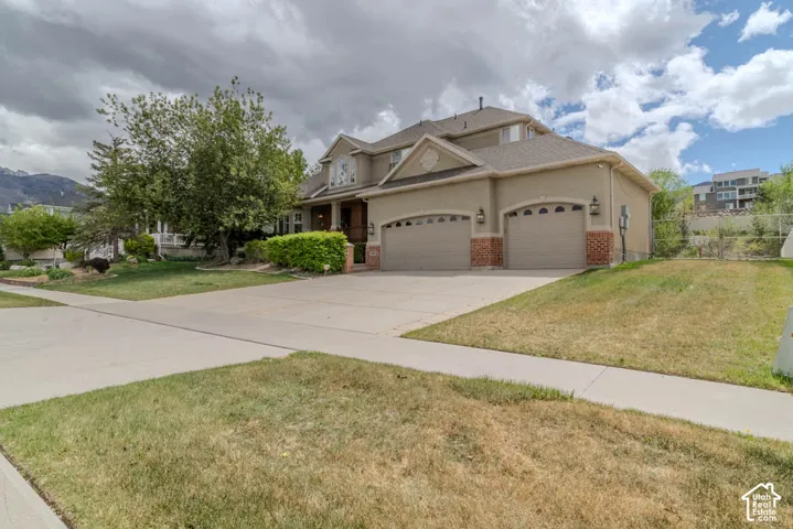 Two-story stucco and brick exterior featuring a two-car garage with arched doors, mature landscaping, and an extended driveway