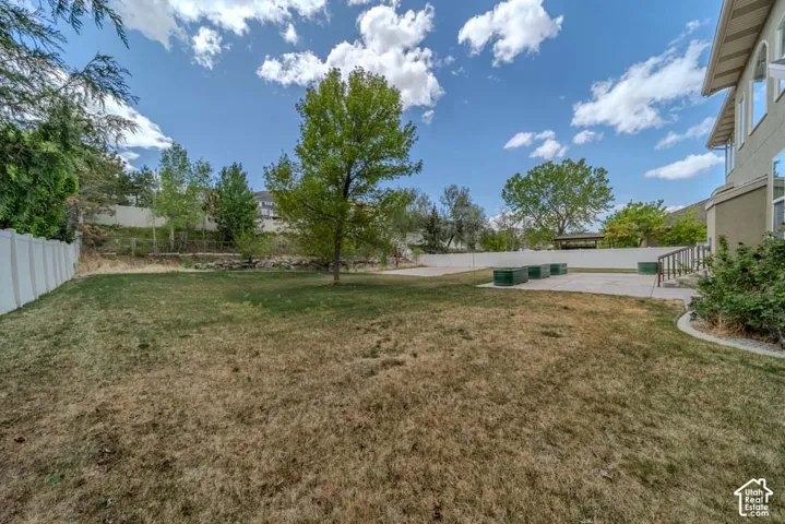 Expansive backyard featuring a concrete patio, a mature tree, and a white perimeter fence