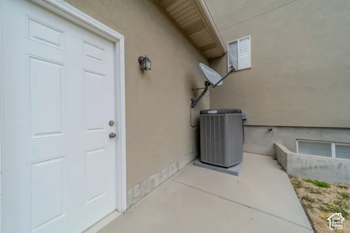 Exterior concrete patio with a white paneled door, wall-mounted light fixture, and HVAC unit