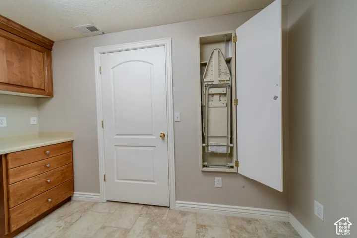 Built-in ironing board cabinet, base and wall cabinetry with wood-finish doors, light-toned countertop, and tile flooring