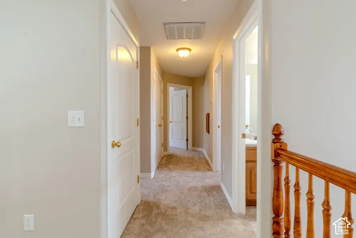 Carpeted hallway featuring light neutral wall paint, white trim, and a classic wood banister