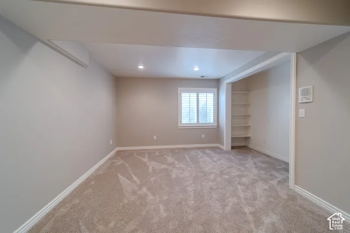 Spacious room featuring plush carpeting, recessed lighting, a window with plantation shutters, an integrated shelving unit, and neutral wall tones