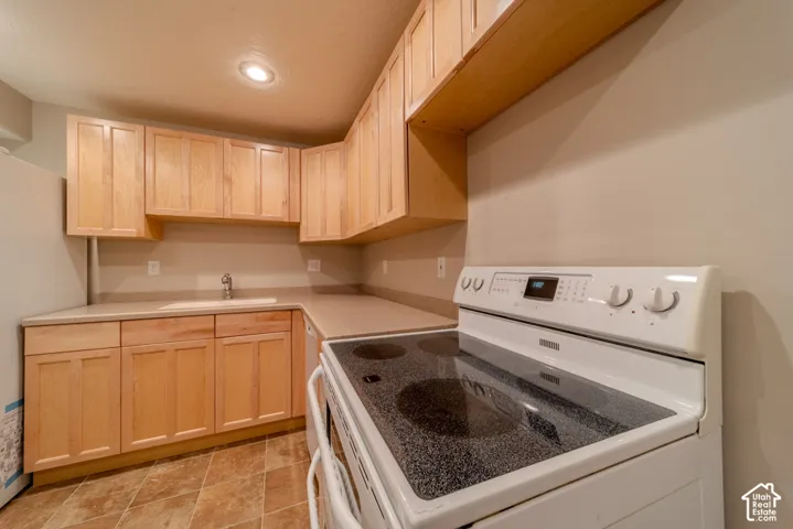 Kitchen featuring light wood cabinetry, neutral countertops, a built-in sink with a single-handle faucet, and a white electric range with a black cooktop