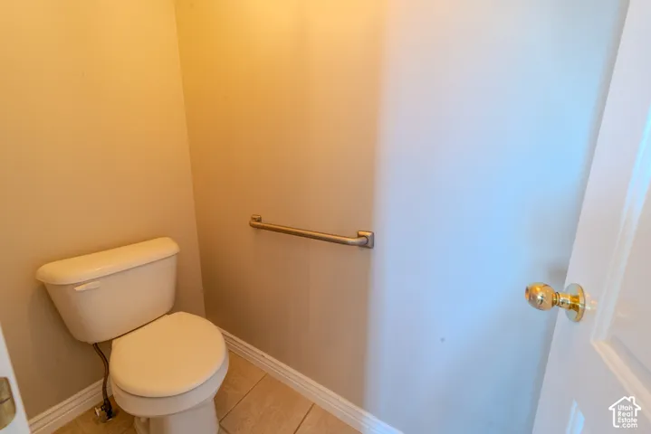 Neutral-toned walls complement the light-colored toilet and floor tiling, featuring a metal grab bar and a white door with a brass-finish knob