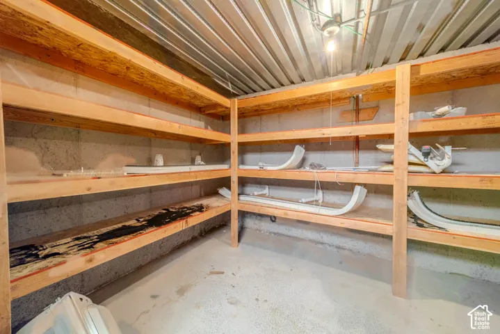 Basement storage area featuring extensive built-in wooden shelving, concrete walls, concrete flooring, and an exposed corrugated ceiling