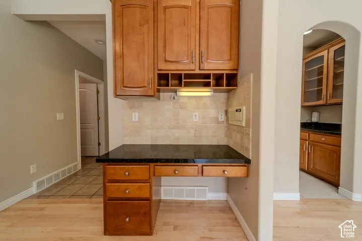 Built-in desk featuring a dark countertop, light wood cabinetry, and a neutral tile backsplash
