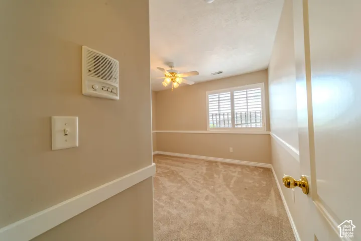 Carpeted room featuring a ceiling fan with light fixture, window with white louvered shutters, and a chair rail molding