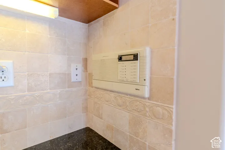 Stone tile backsplash with decorative border detailing, integrated intercom system, under-cabinet lighting, and dark countertop