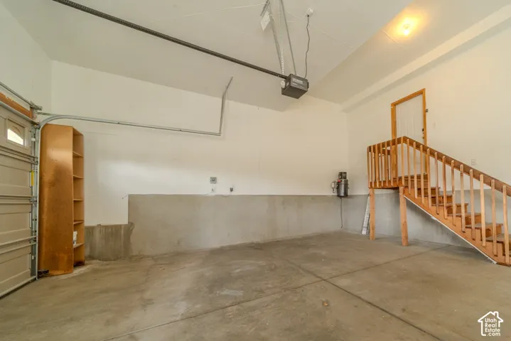 Spacious garage with a concrete floor, white painted walls, exposed ceiling joists, and an automatic garage door opener