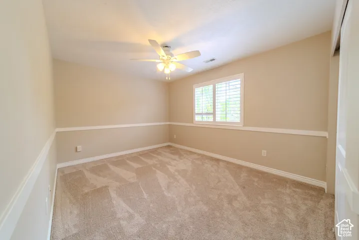Carpeted room featuring a ceiling fan with light fixture, window with plantation shutters, chair rail molding, and neutral wall tones