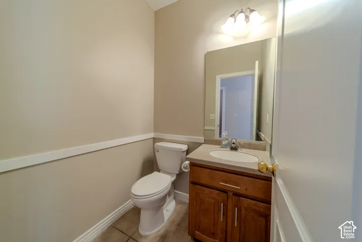 Powder room featuring a single-basin vanity with a wood-finish cabinet, a built-in mirror, a flush-mount light fixture, and tile flooring