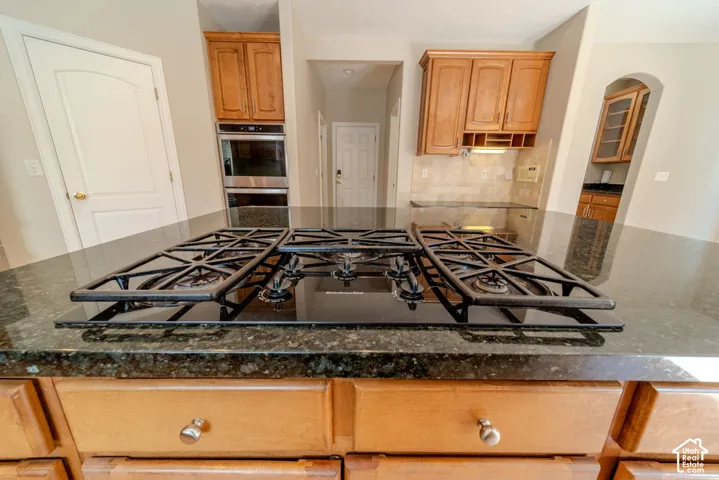 Kitchen island featuring a black gas cooktop with grates, surrounded by a dark granite countertop