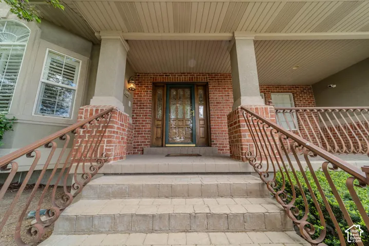 Covered brick entry with an ornate wood-paneled door featuring decorative glass inserts, complemented by detailed iron railings and textured paver steps