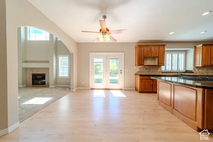 Open-concept living space featuring light wood-finish flooring, a kitchen with wood cabinetry and dark countertops, and a living area with a fireplace and vaulted ceilings