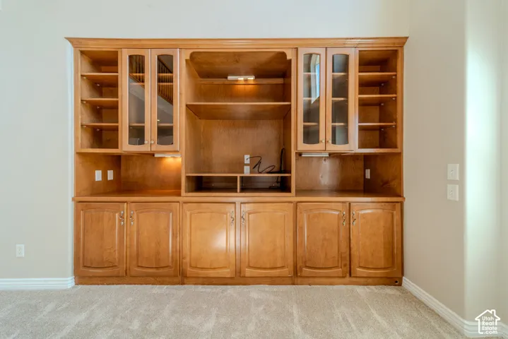 Integrated wood-finish entertainment center with extensive shelving, glass-front cabinetry, under-cabinet lighting, and lower storage cabinets
