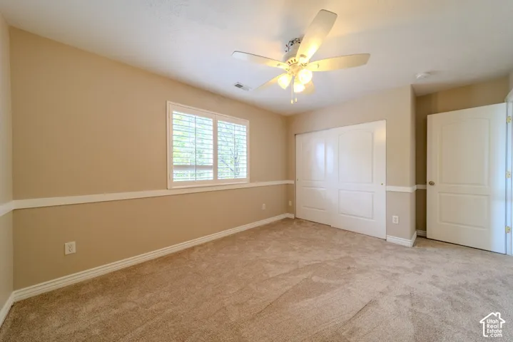Carpeted room with a ceiling fan light fixture, white plantation shutters, a two-tone wall finish with chair rail molding, and a sliding closet door
