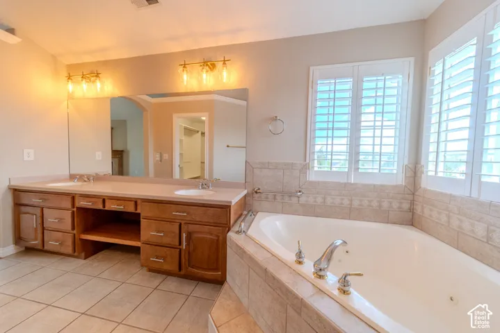 Spacious bathroom featuring a built-in soaking tub with surrounding tile, plantation shutters, and a double vanity with ample storage